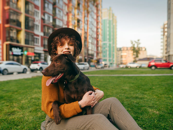 Smiling woman sits on the lawn with her dog in the city