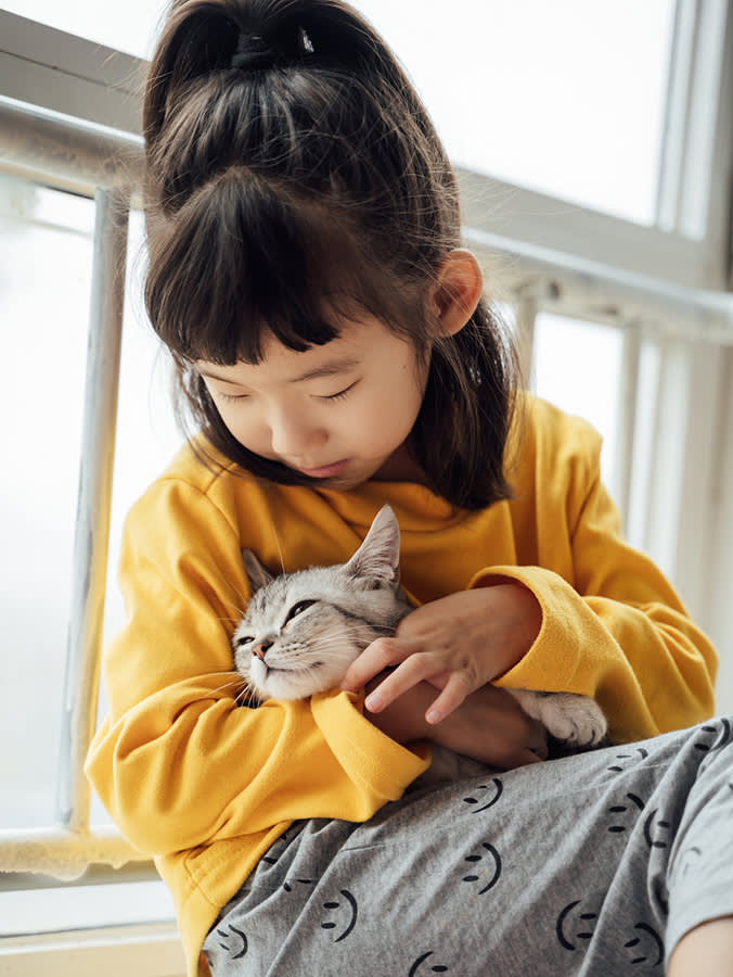 Cute little girl playing with her pet kitten at home.