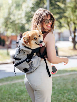 Woman carrying a dog in a backpack outside.