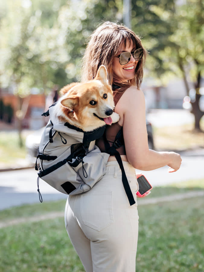 Woman carrying a dog in a backpack outside.