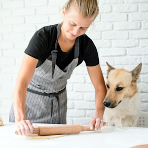 Woman rolling out dog treat dough while her dog watches.