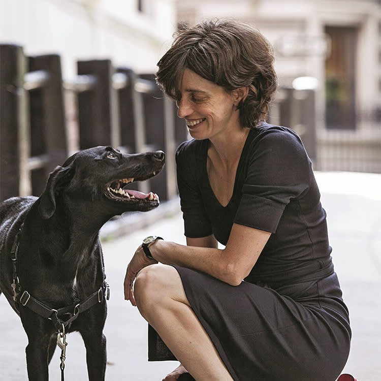 A woman kneeling down while smiling at her dog. 