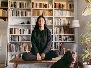 Woman meditating with her chocolate lab in the living room.