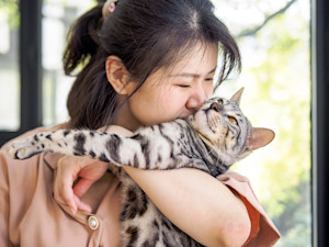 Woman trying to hold her cat in a hug.