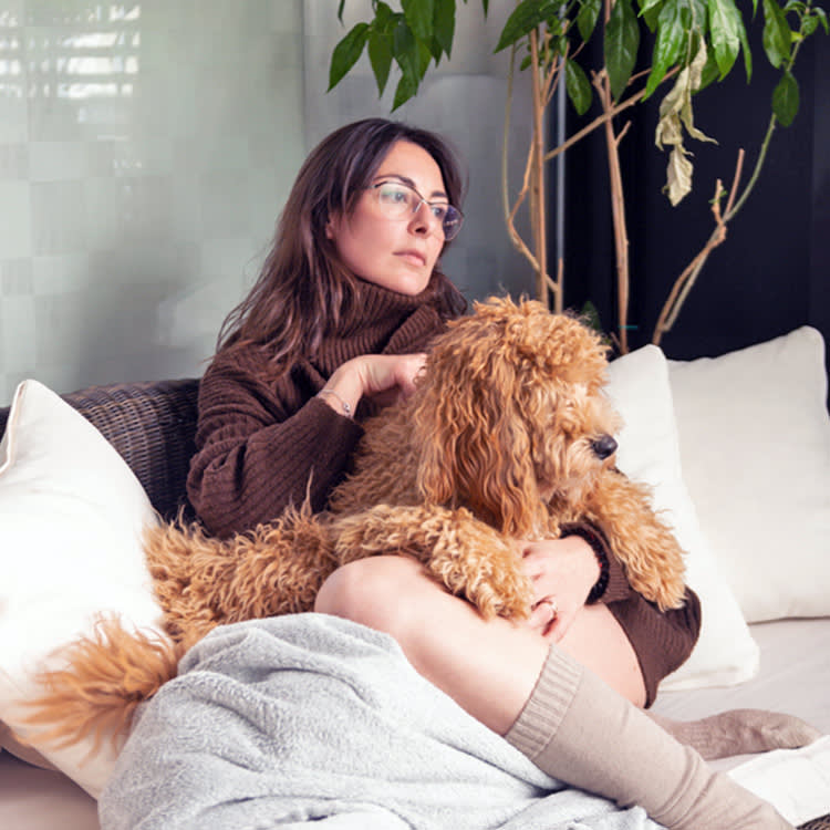 Sad woman sitting on her couch with her brown poodle dog.