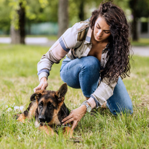 Young woman comforting German Shepherd puppy outside.