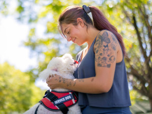dog wearing service dog tabard jumps up at girl with brown hair and tattoos