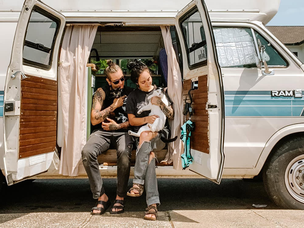 Gene and Shay sitting int he open side of their van home while holding both of their cats