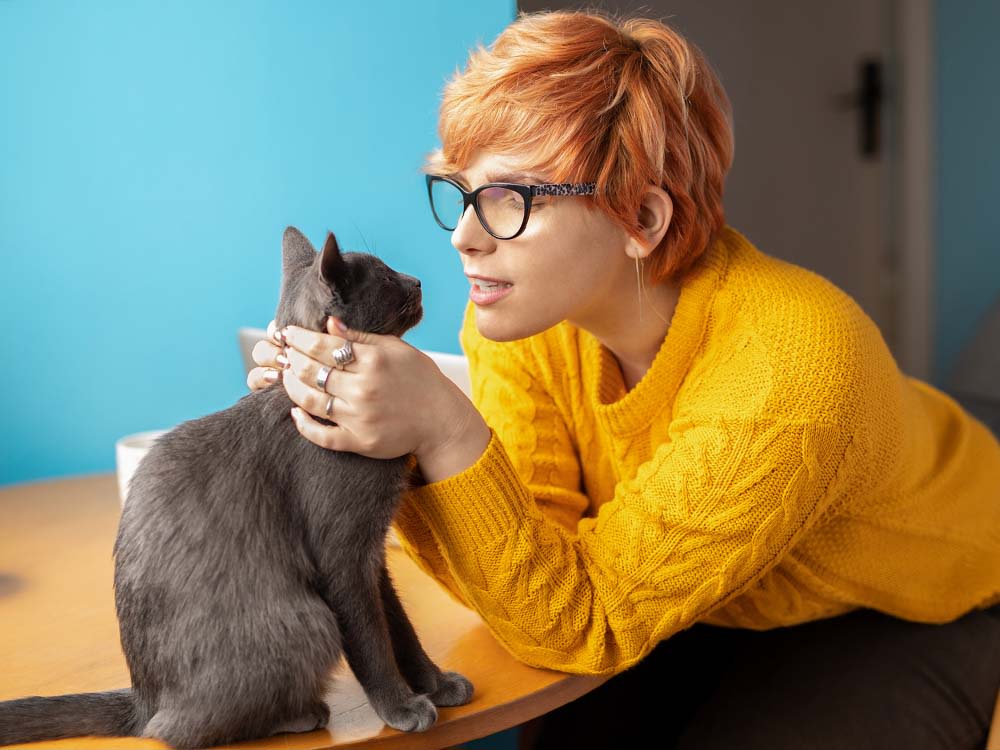 Red haired woman in bright yellow sweater talking to her dark grey cat