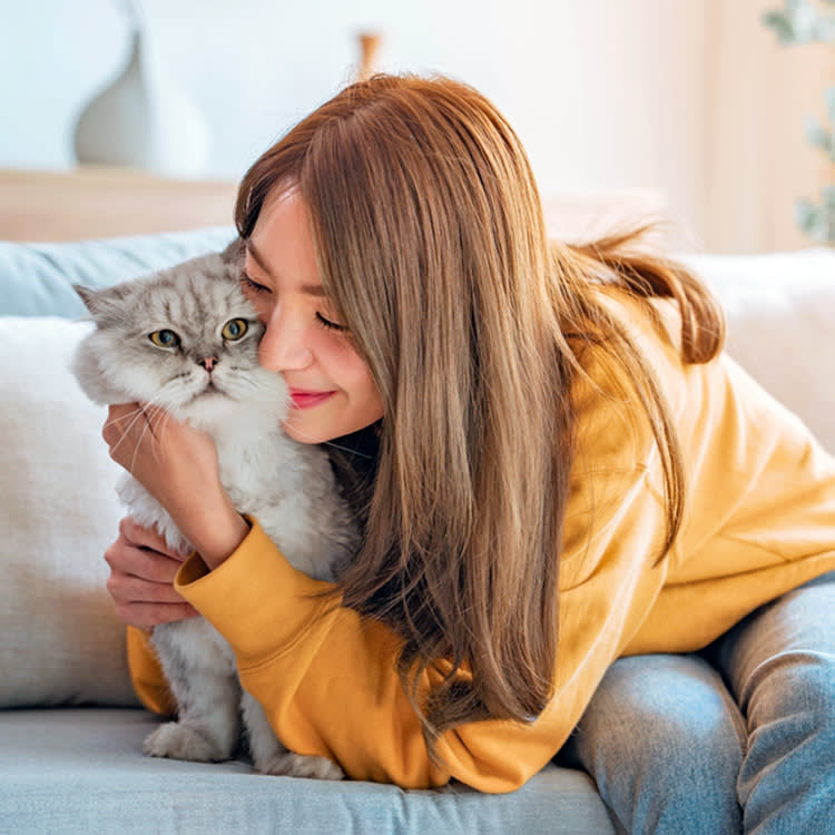 Woman snuggling her cat at home on the couch.