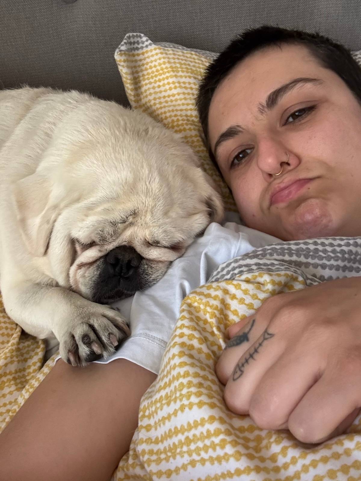 a picture of a person with a grumpy face cuddling up to a Pug in bed