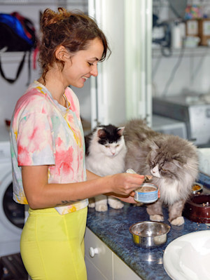 Woman feeding her cats at home.