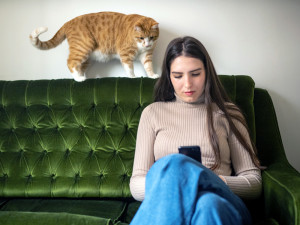Woman on her phone sitting on couch while cat watches.