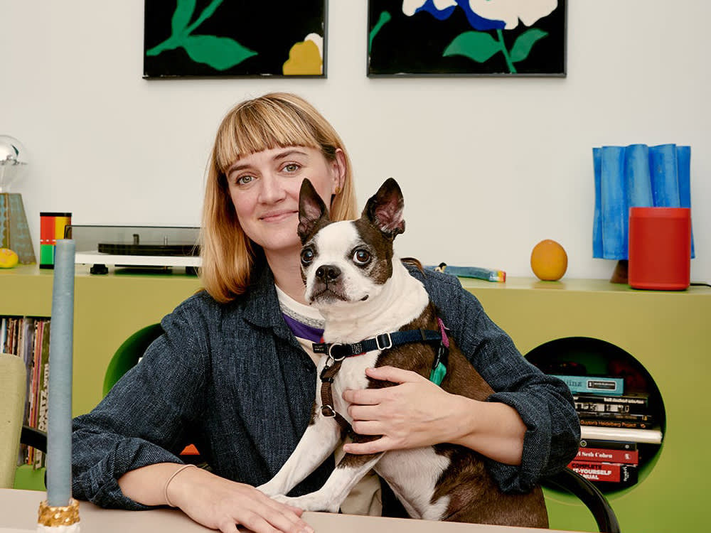 Ellen Dusen holding her dog Snips while seated at a colorful table