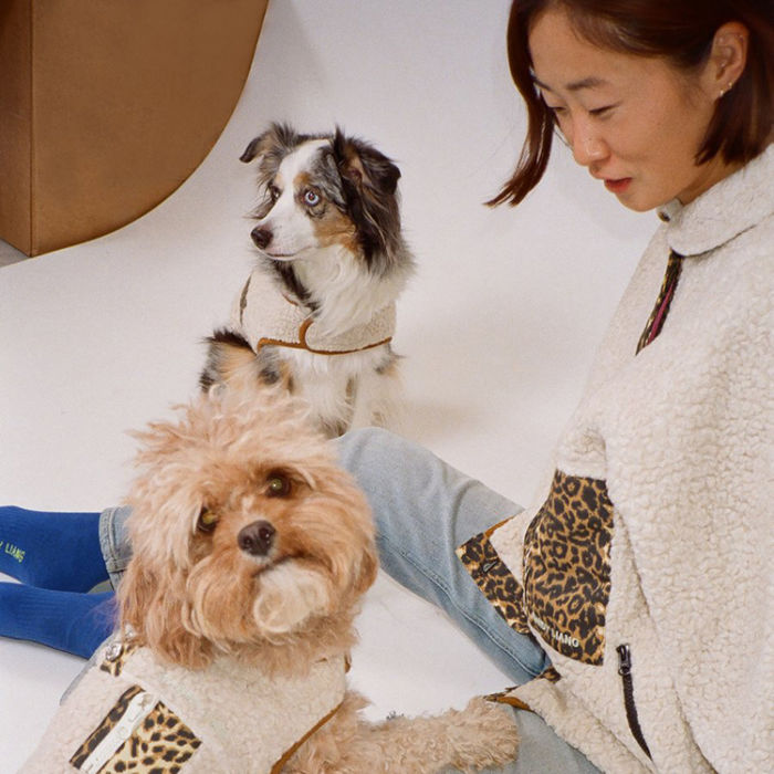 Sandy Liang wearing a matching cream colored fleece with a cheetah print accent looking down at two dogs wearing matching sweaters
