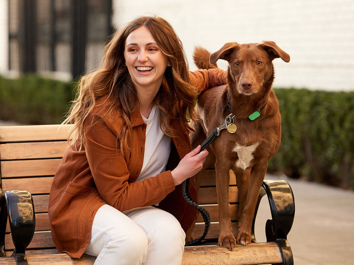 A woman laughing while sitting on a bench with her dog.