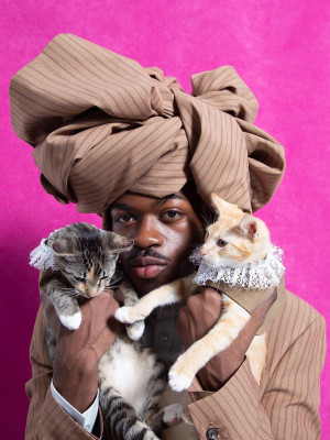 Man holding two cats with clothes on.