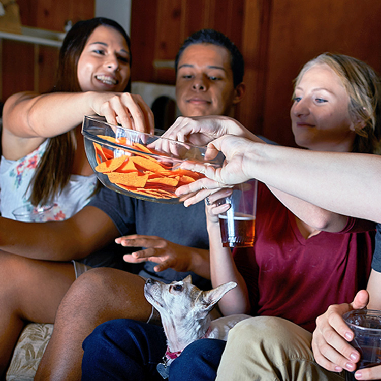 Group of friends eating Doritos chips at home with their dog.