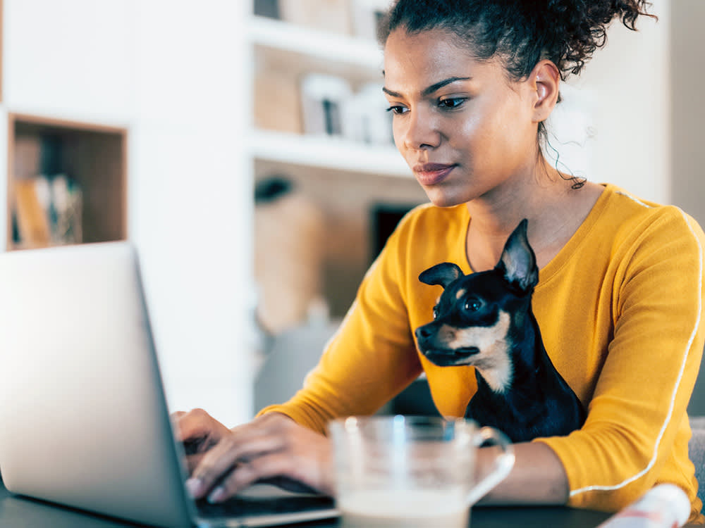 Young woman sitting with her pet dog and using laptop at home.