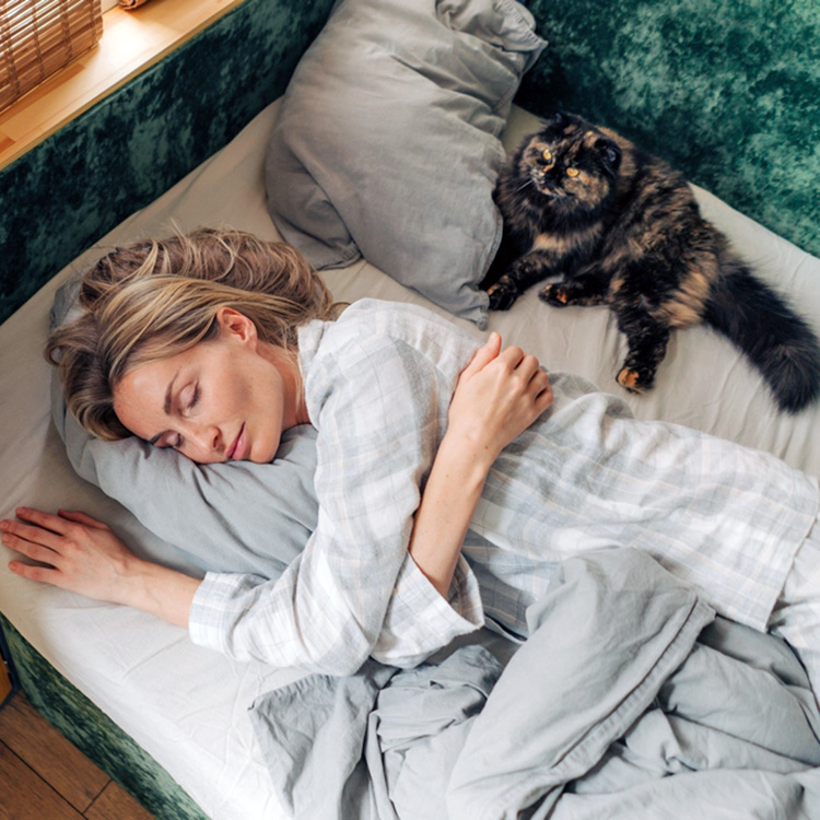 Cat watching woman sleep in bed.