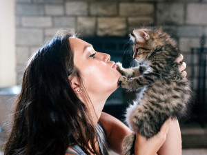 Woman holding brown kitten to her face.