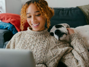 A woman staring at her computer while holding her dog close. 