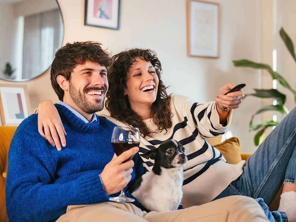 Couple watching tv with their dog at home.