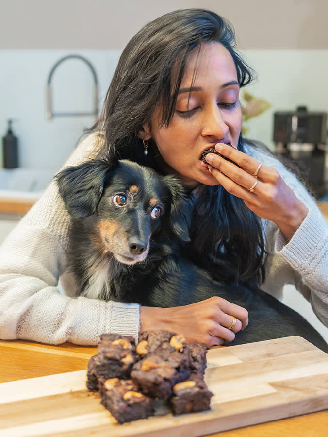 Woman eating brownies in front of her dog at home.