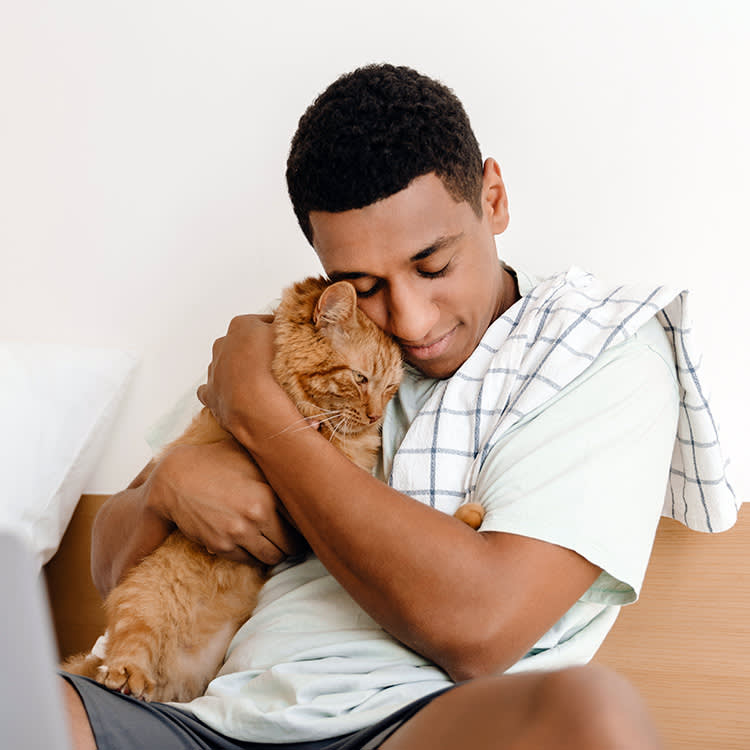 Man cuddling a cat in his lap at home.