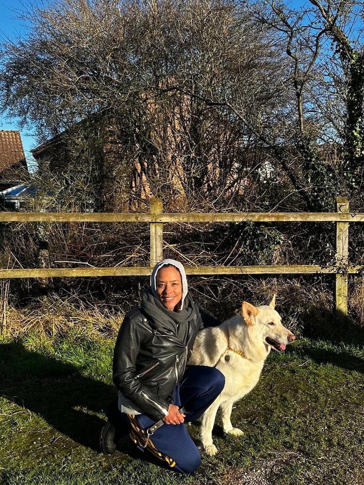 a picture of a woman in a field crouching down with a big white fluffy dog