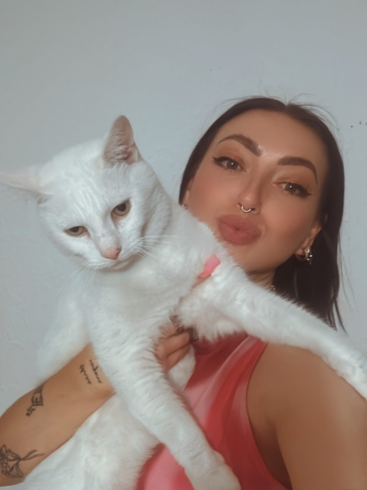 a woman blows a kiss at the camera while holding up a white cat
