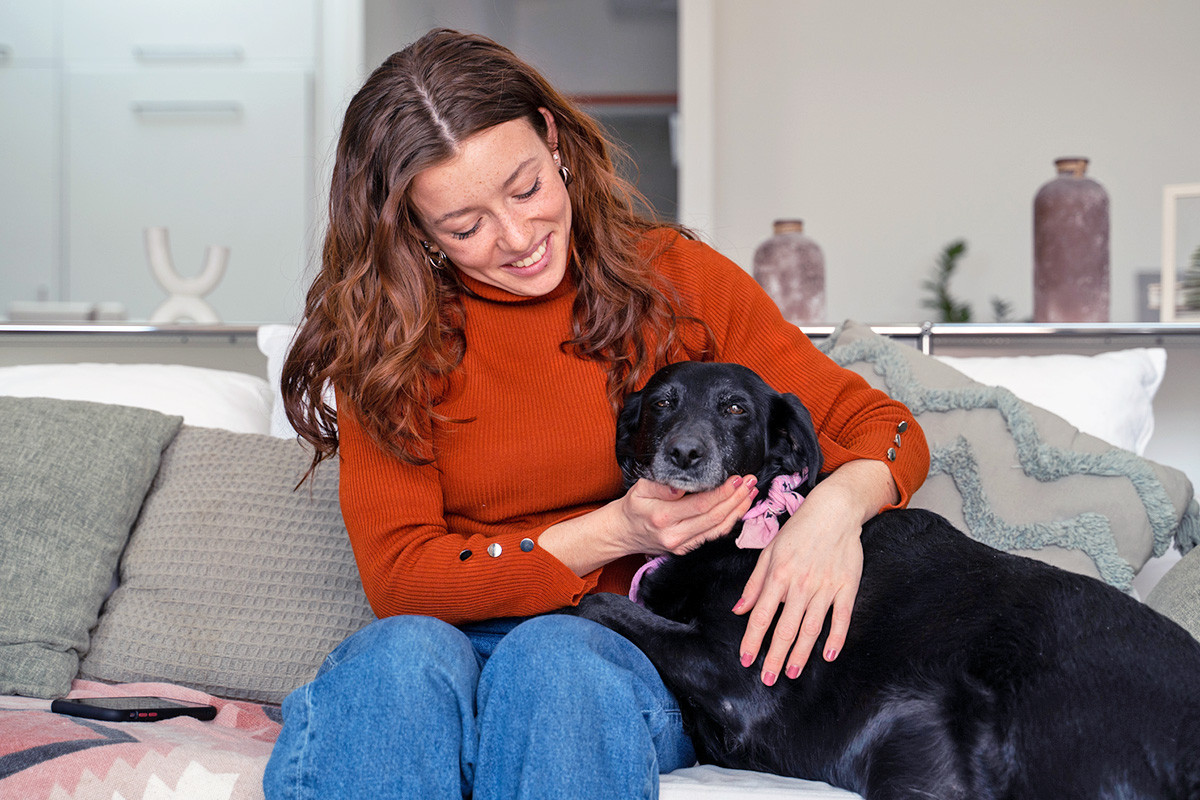 woman cuddles with dog on couch