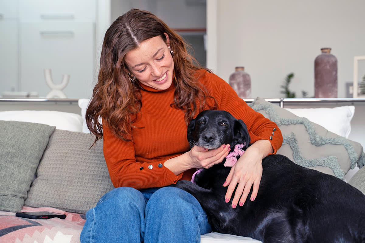 woman cuddles with dog on couch