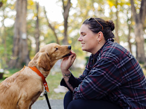 Woman training her golden retriever puppy outside.