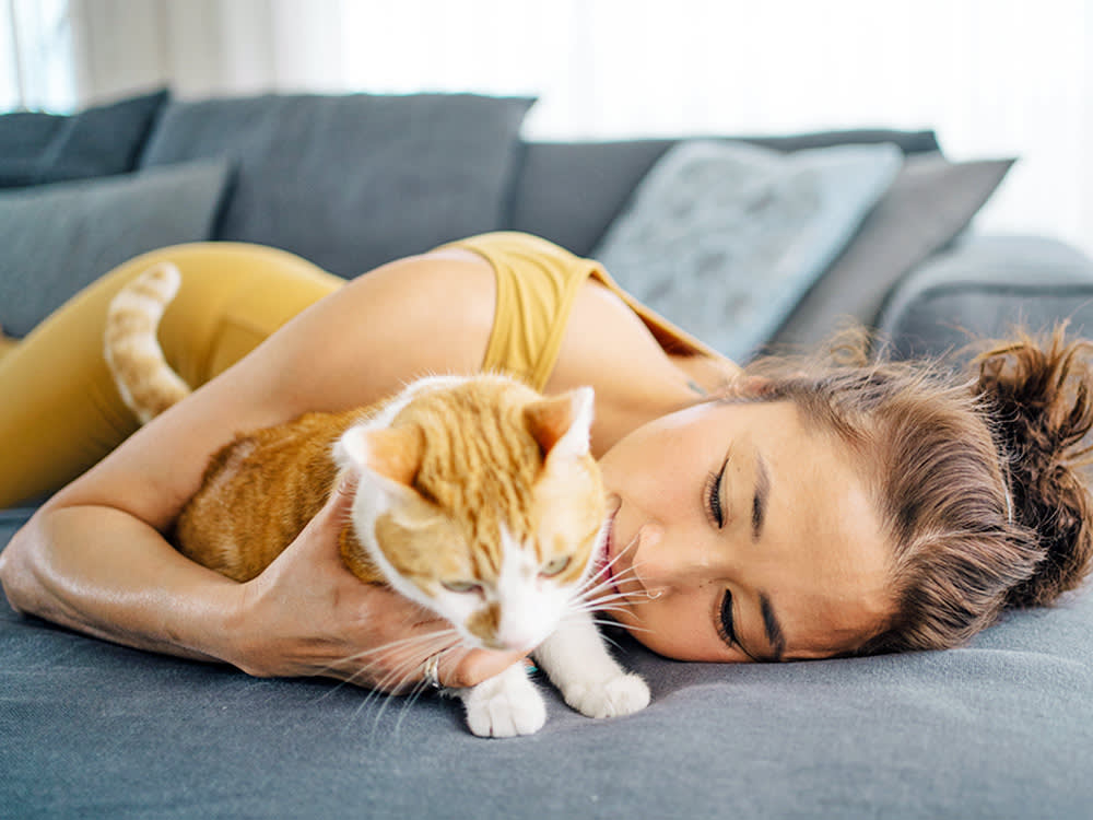 Woman cuddling her cat on the couch at home.
