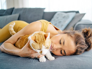 Woman cuddling her cat on the couch at home.