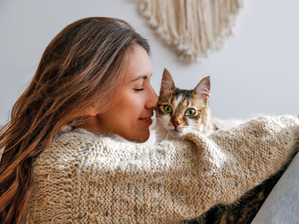 Picture of a woman with brown hair hugging a cat