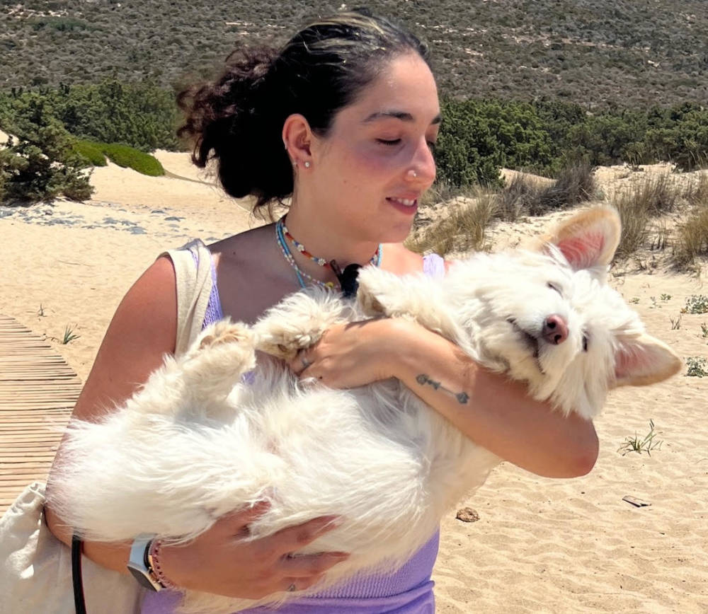 a woman with black hair hugs her white fluffy dog 