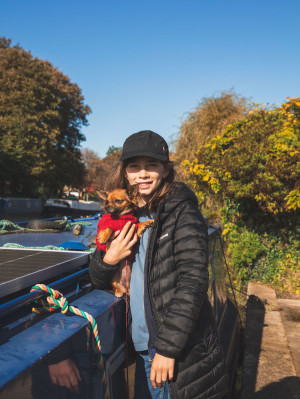 a boy cuddles a small dog while standing next to a narrowboat