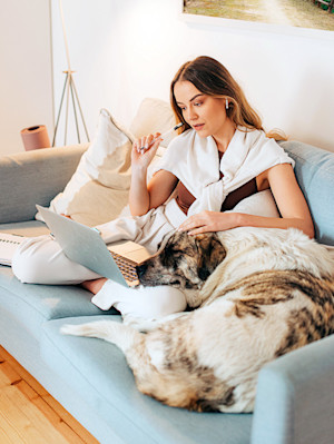 Woman on sofa with laptop and dog cuddling