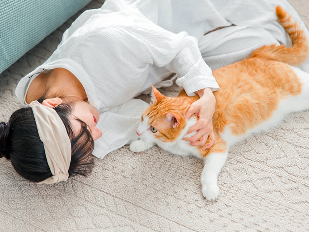 Woman lies on carpet with orange cat.