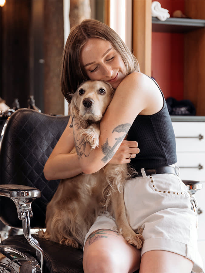 Young smiling female owner sitting on leather chair and embracing cute beige Cocker Spaniel dog.