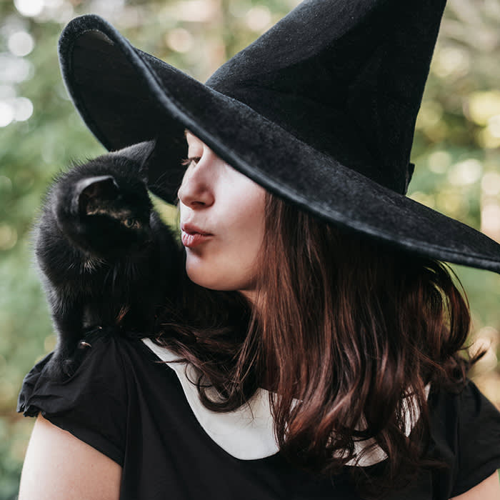 a person dressed up as a witch, kissing her cat