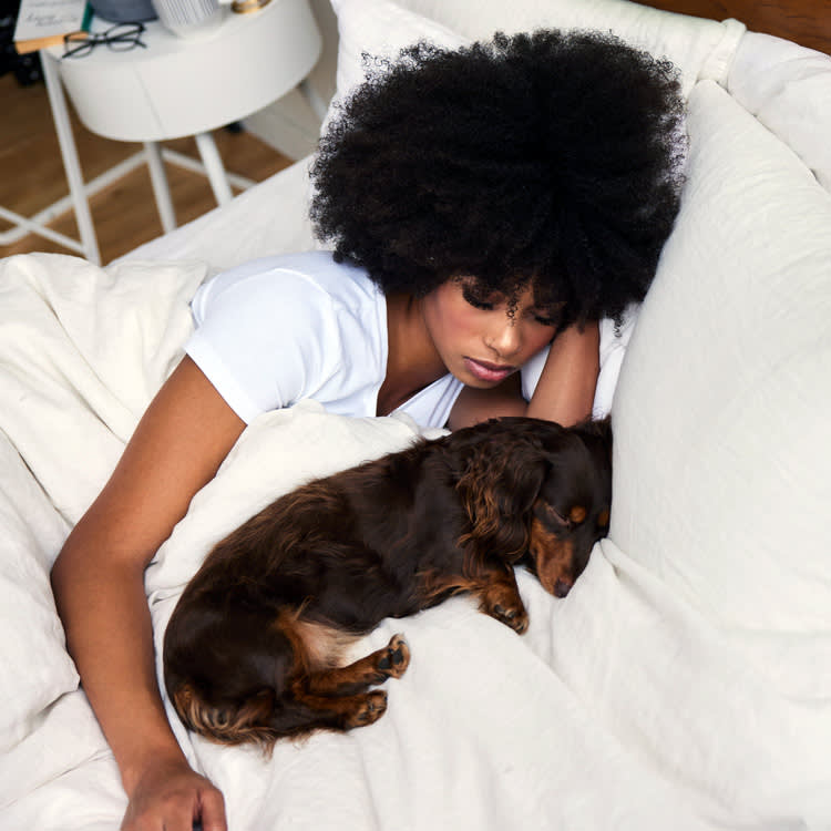 woman with black curly hair sleeping in bed with her long hair daschund