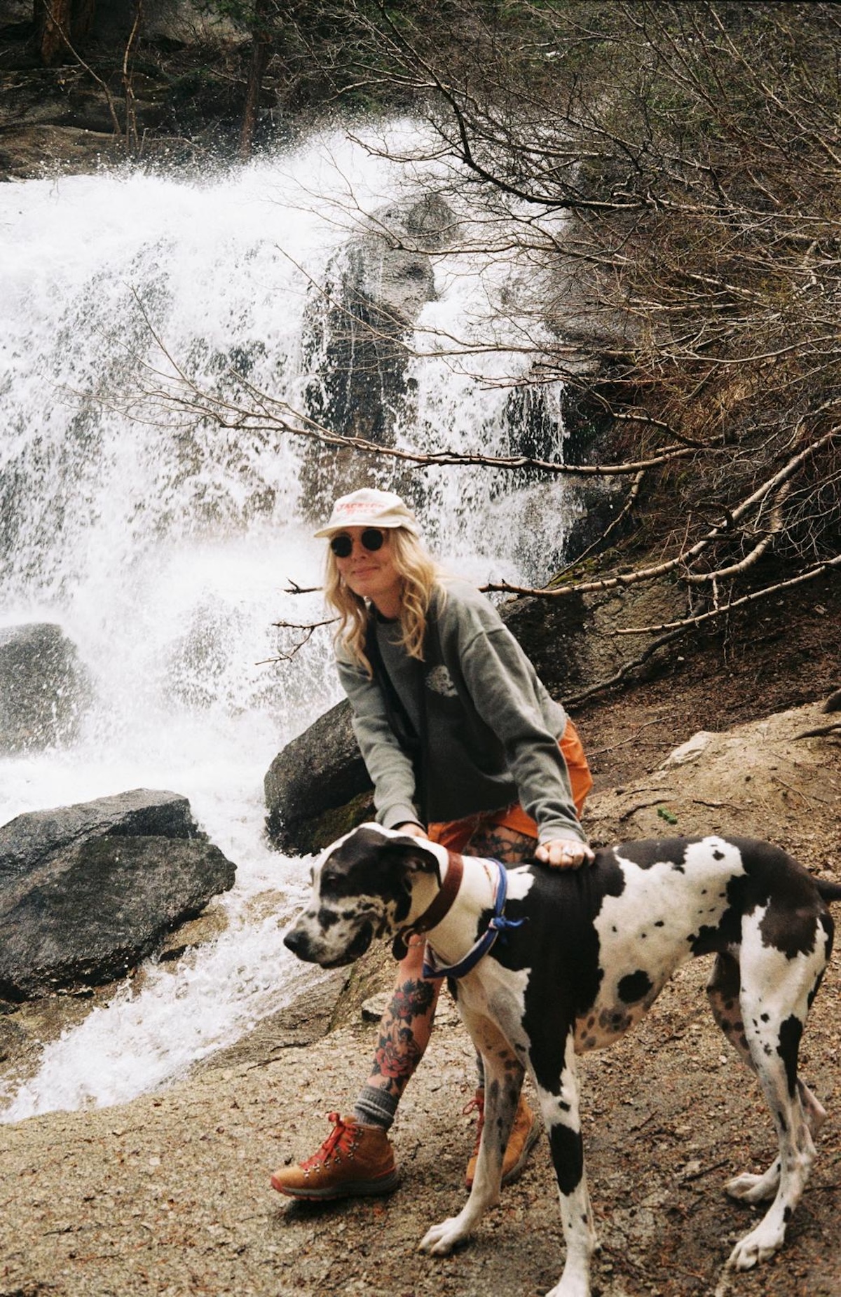 a picture of a blonde lady hiking by a waterfall with a large black and white great dane dog