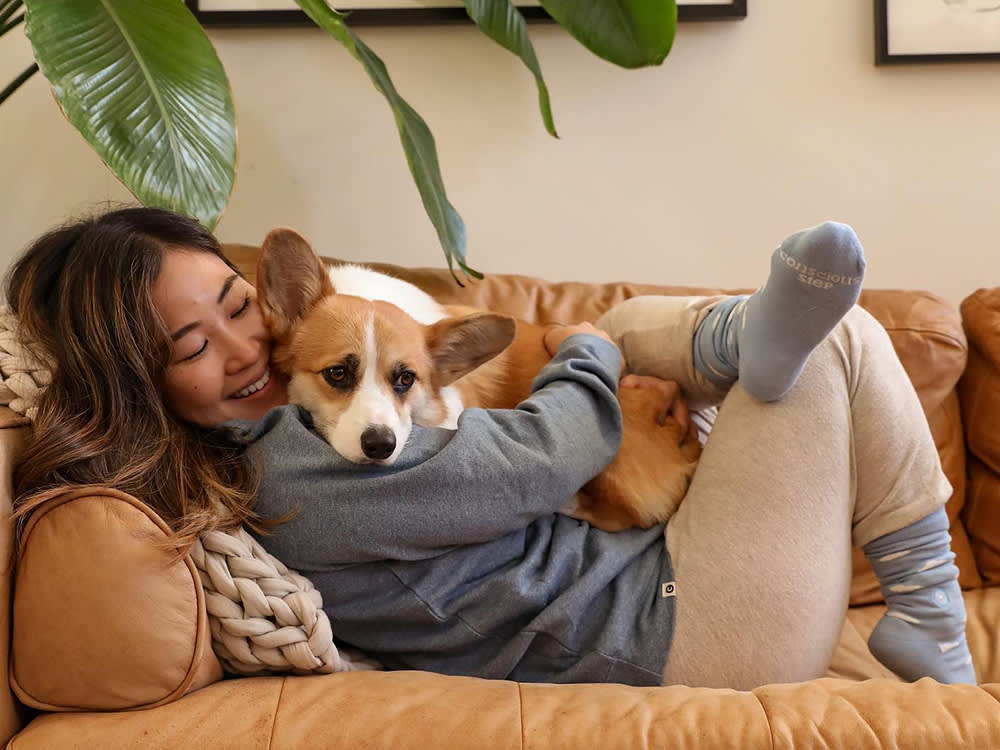 Minna Lee smiling at the camera while holding her dog, Benny the Corgi, who is dressed in a Sherlock Holmes Halloween costume