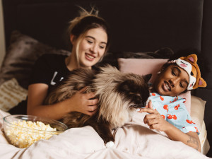 Two girls have a sleepover with a fluffy cat and a bowl of popcorn.