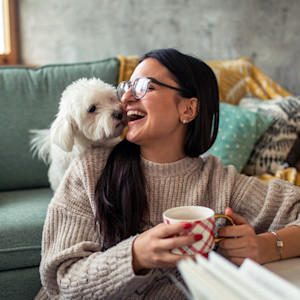 Young woman drinking tea while playing with her dog at home