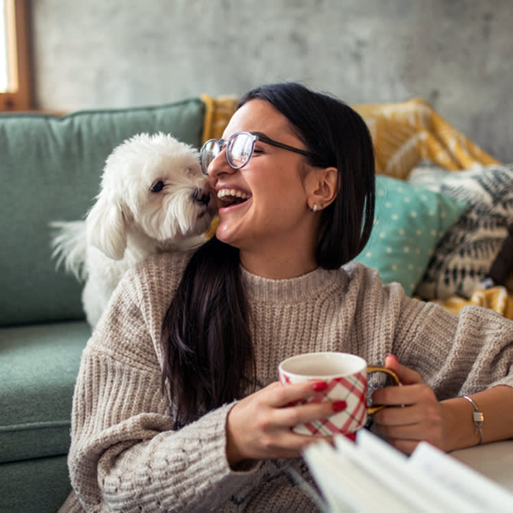 Young woman drinking tea while playing with her dog at home