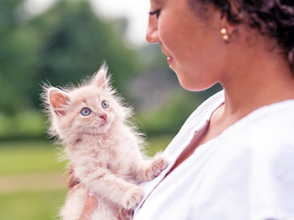 Woman holding her young kitten in her arms outside.